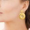 Boucles d'oreille pendantes Ariel, motif double disque ajouré en acier pvd doré texturé. Présentées portées.