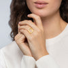 Bague Gina, motif irrégulier ovale, sur corps de bague fil demi-jonc réglable.
En acier PVD doré. Présentée portée.