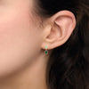 Boucles d'oreille composées de 2 motifs en pierres synthétiques vertes de forme poire et rond, serti clos perlé, plaqué or 750 millièmes. Représentées portées.